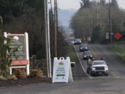 Traffic traveling on Northeast 119th Street passes signs advertising homes for sale. The area around the street has been growing, and the roadway is now being improved to keep up.