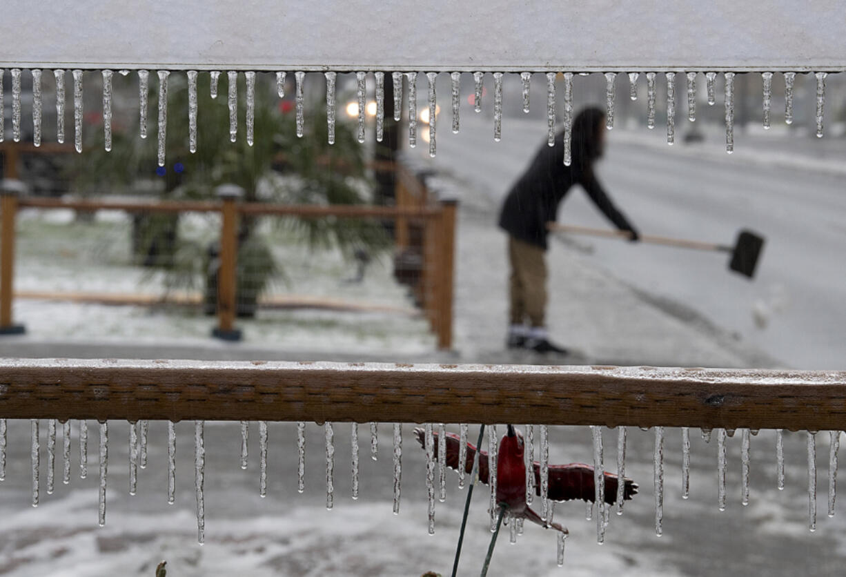 Icicles hang from a yard sign as Gloria Winner, 13, shovels ice from the sidewalk outside her Vancouver home to make the area safer for pedestrians Friday afternoon.