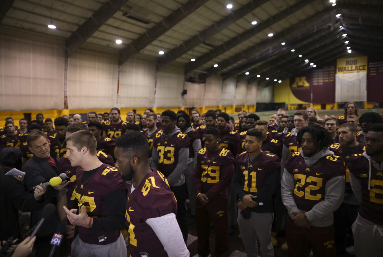 University of Minnesota wide receiver Drew Wolitarsky, flanked by quarterback Mitch Leidner, obscured behind Wolitarsky, and tight end Duke Anyanwu gestures as he stands in front of other team members while talking to reporters in the Nagurski Football Complex in Minneapolis, Minn., Thursday night, Dec. 15, 2016.  The players delivered a defiant rebuke of the university's decision to suspend 10 of their teammates, saying they would not participate in any football activities until the school president and athletic director apologized and revoked the suspensions. If that meant they don't play in the upcoming Holiday Bowl against Washington State, they appeared poised to stand firm.