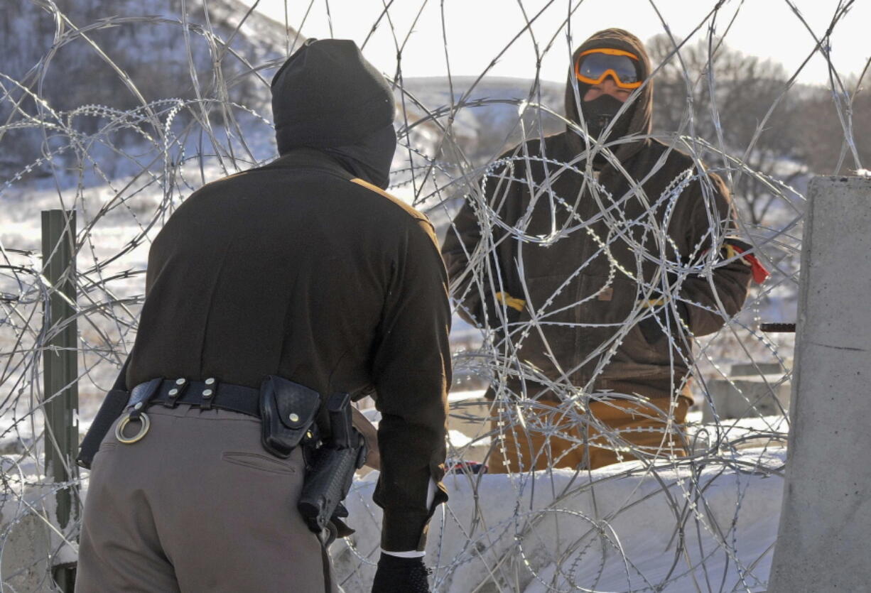 A law enforcement officer speaks to an oil pipeline protester through a wall of razor wire Dec. 8 on the Backwater Bridge in southern Morton County, N.D.