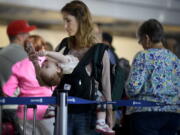 Ann Walden checks her phone as 15-month-old daughter Delphine plays while waiting in line after their flight was delayed Sept. 26, 2014, at O&#039;Hare International Airport in Chicago. There are several ways to distract and soothe little ones when traveling by air.