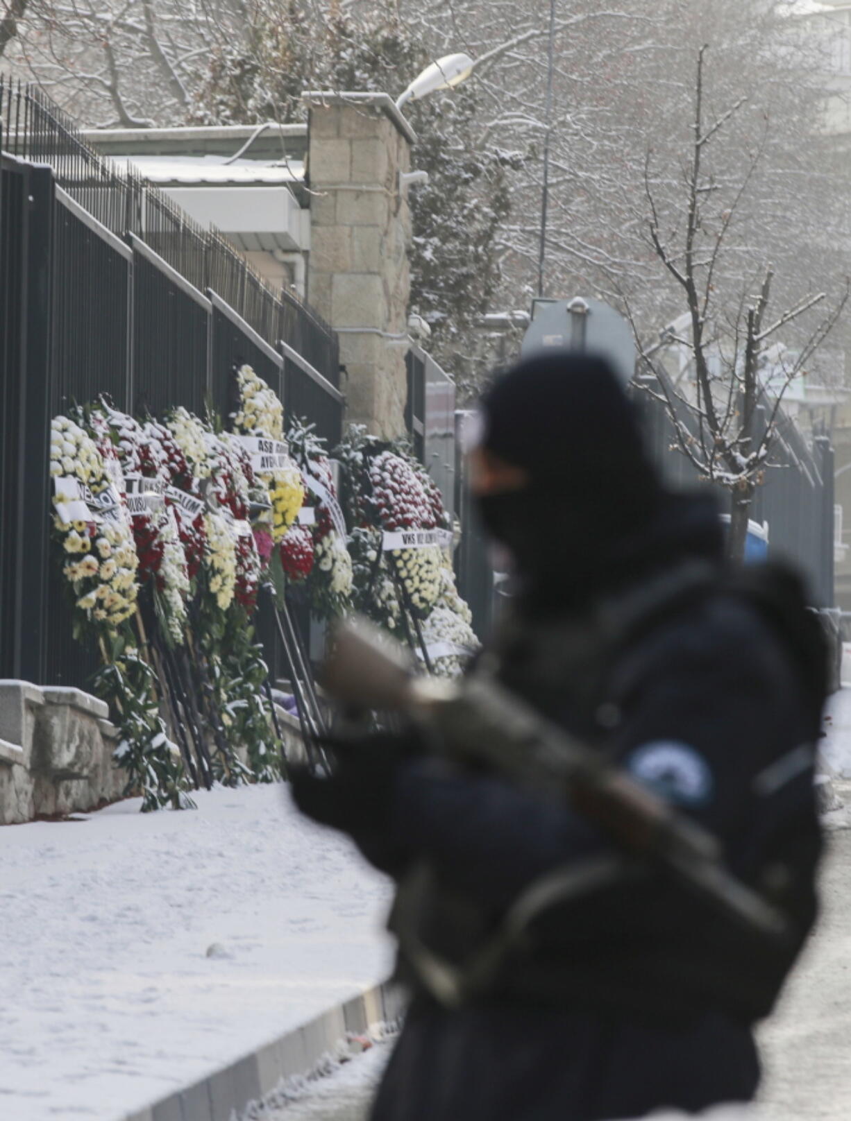 Wreaths are left on the the road leading to the Russian embassy in Ankara, Turkey, Wednesday, Dec, 21, 2016, as a Turkish police officer secures the road. Russian Ambassador to Turkey, Andrei Karlov, was assassinated Monday by a police officer during the opening of a photo exhibition.