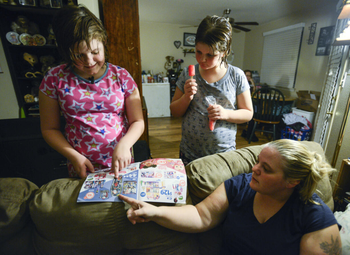 Sisters Kaylynn, left, and Emily Ward look at newspaper advertisements with their mom, Ginger Marcom, at Marcom&#039;s sister&#039;s apartment in Vancouver in November. The family has been staying with friends and family after Marcom&#039;s former landlord sold the property they were renting and gave them less than 30 days to move. Marcom recently found a home that will accept her Section 8 housing voucher, but is struggling to afford the deposit.