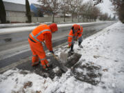 Howard Taylor, left, and Gavin Craig of the Vancouver Department of Public Works stormwater division clear snow from storm drains along Southeast 20th Street on Tuesday afternoon. Top, a pedestrian on Tuesday afternoon navigates an icy street made more slippery by a thin layer of freezing rain in southeast Vancouver.