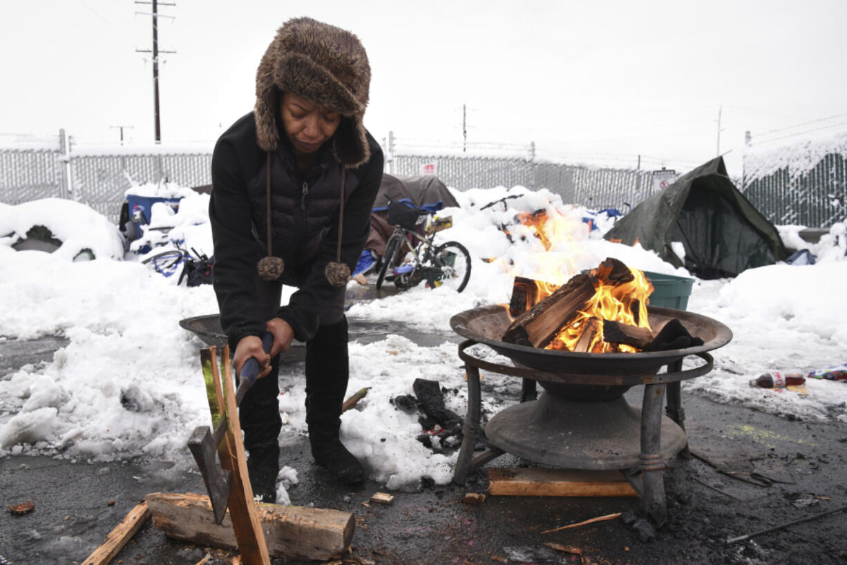 Tiffany Singleton chops firewood outside her tent on West 12th Street in Vancouver on Wednesday. After nearly a foot of snow hit Vancouver Tuesday evening, those living on the streets near the Share House were welcomed Wednesday afternoon by volunteers passing out warm beverages, coats and gloves.