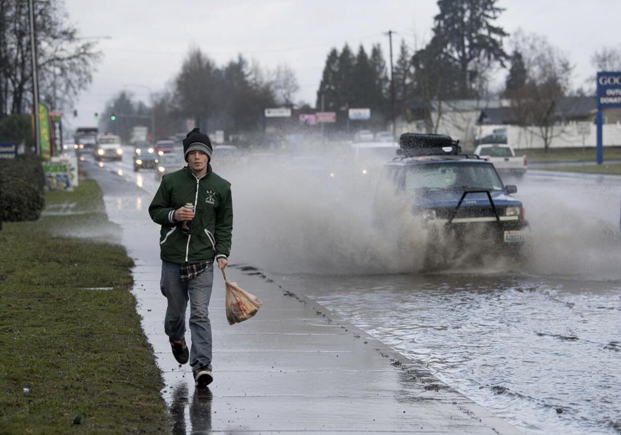 Vancouver resident Joshua King jogs to stay ahead of the spray as traffic plows through standing water Wednesday morning along Northeast 117th Avenue. The roadway is also known as state Highway 503.