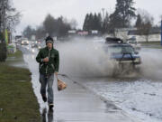 Vancouver resident Joshua King jogs to stay ahead of the spray as traffic plows through standing water Wednesday morning along Northeast 117th Avenue. The roadway is also known as state Highway 503.