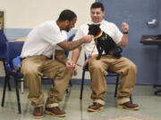 Darion Chambers, left, and Christopher Baker, both inmates at Larch Corrections Center, give treats to Ricky, a 3-year-old Chihuahua mix. Ricky is from the Humane Society for Southwest Washington, which partners with the prison to offer a program that allows inmates to train dogs.