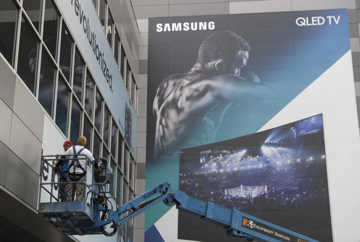 Workers hang up a sign near a Samsung TV banner during setup for CES International on Tuesday in Las Vegas. The show runs through Sunday.