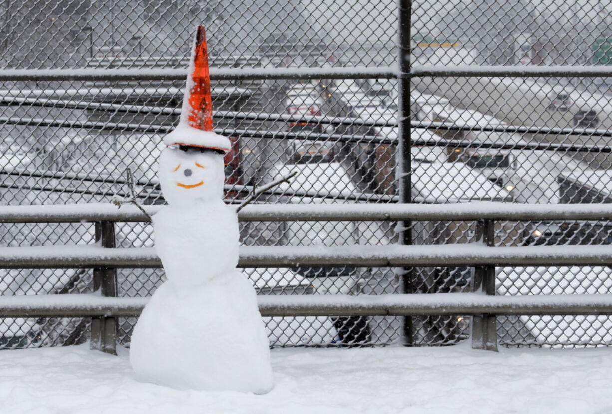 A snowman wearing a traffic cone hat is shown on an overpass as early morning traffic is at a standstill in the background on Interstate 5 headed into Portland, Wednesday, Jan. 11. A snowstorm spread through Portland and parts of Washington state overnight, toppling trees, closing schools and cutting power to thousands.