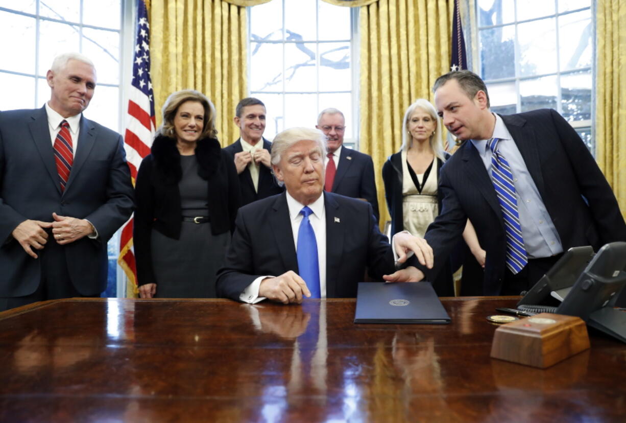 President Donald Trump is handed an Executive Order to sign by White House Chief of Staff Reince Priebus, right, with Vice President Mike Pence, left, and others nearby, in the Oval Office of the White House on Saturday in Washington.