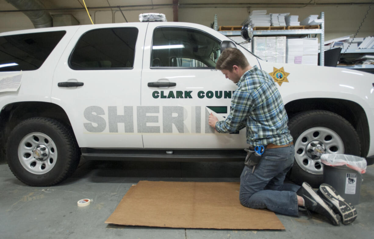 Kai Crown applies decals to sheriffs&#039; office vehicles at International Graphics and Nameplate in Vancouver.