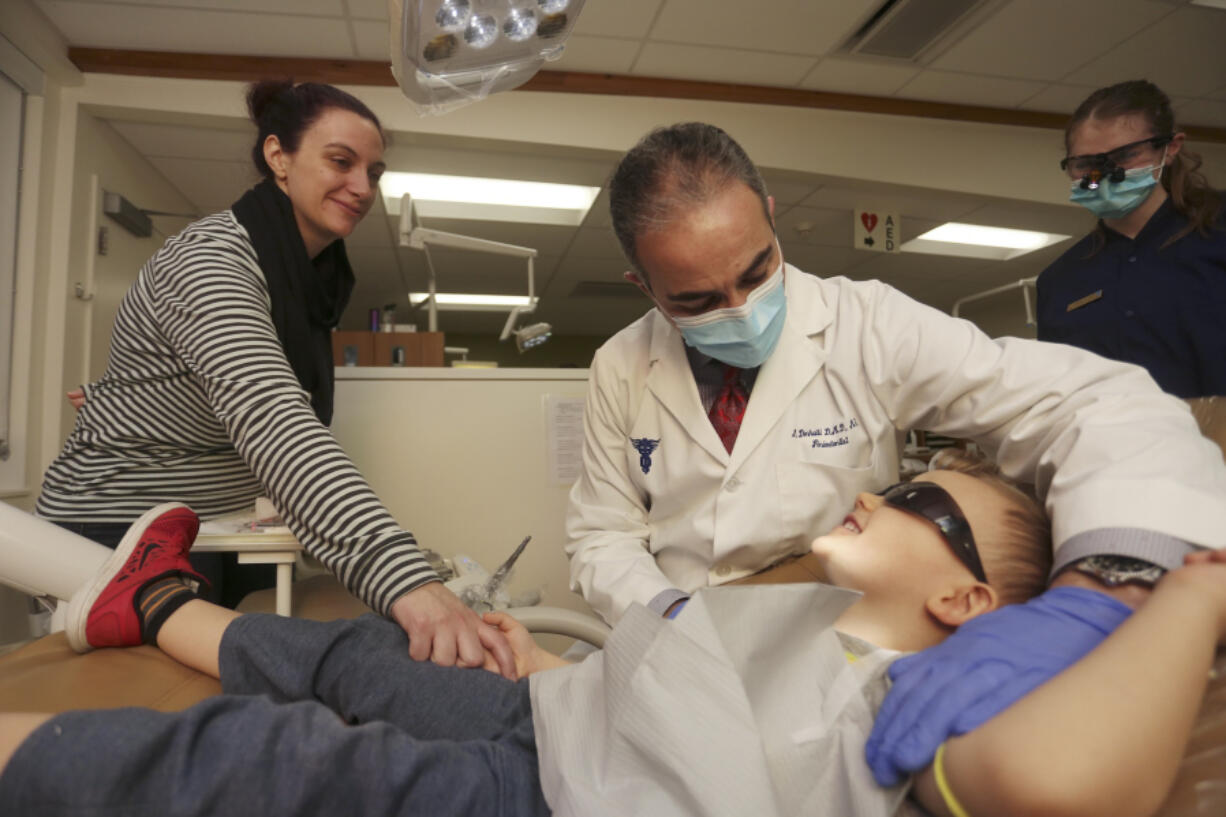 Volunteer dentist Dr. Munib Derhalli, center, checks 3-year-old Brendan Shiemke&#039;s teeth while his mother, Dallas Shiemke, holds his hand for support during the Clark College Dental Hygiene Program&#039;s free children&#039;s dental clinic Saturday.