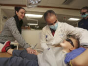 Volunteer dentist Dr. Munib Derhalli, center, checks 3-year-old Brendan Shiemke&#039;s teeth while his mother, Dallas Shiemke, holds his hand for support during the Clark College Dental Hygiene Program&#039;s free children&#039;s dental clinic Saturday.