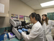 Microbiologist Lillian McLitus, center, inserts a sample into the new DNA testing machine as OHSU lab student Lue Ann MacKenzie looks on at PeaceHealth Southwest Medical Center in September.