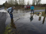 Battle Ground&#039;s Frank Alarcon, left, tries Monday to dislodge a garbage can blocking a drainage ditch in front of his home with the help of passer-by Herschel Gaskill in northeast Battle Ground. They succeeded, and water started to drain properly.