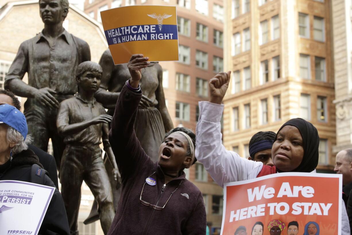 Julie Gonzalez, of Boston, center, and Sadia Mohamed, of Chelsea, Mass., right, display placards and chant slogans while standing in front of a memorial to the Irish potato famine, left, during a rally called "We Will Persist," Tuesday, Feb. 21, 2017, in Boston. According to organizers the rally was held to send a message to Republicans in Congress and the administration of President Donald Trump that they will continue to press for immigration rights and continued affordable healthcare coverage.