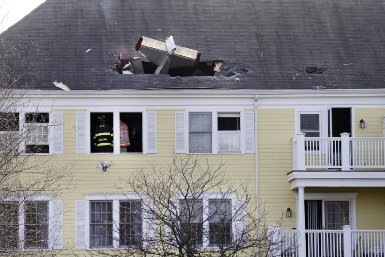 Firefighters investigate the scene Tuesday after a small plane crashed into the roof of a condominium building across the Merrimack River from Lawrence Municipal Airport, in Methuen, Mass. According to police, the pilot of the home-built plane was killed.