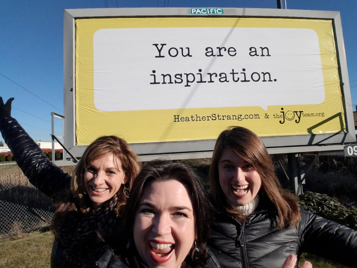 The Joy Team&#039;s Chief Joy Officer Michele Larsen, center, with co-workers Leanne Reid, left, and Megan Streeter in front of one of the organization&#039;s older billboards in Vancouver.