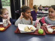 Burton Elementary School kindergartner Josephine Liambila, center, takes a bite of a roasted potato wedge during lunch Monday while classmates Ashlynn Miller, left, and Silvia Paunescu, right, watch. Potatoes were the Harvest of the Month, an in-season, regionally grown food that was prepared and sampled by elementary school students.