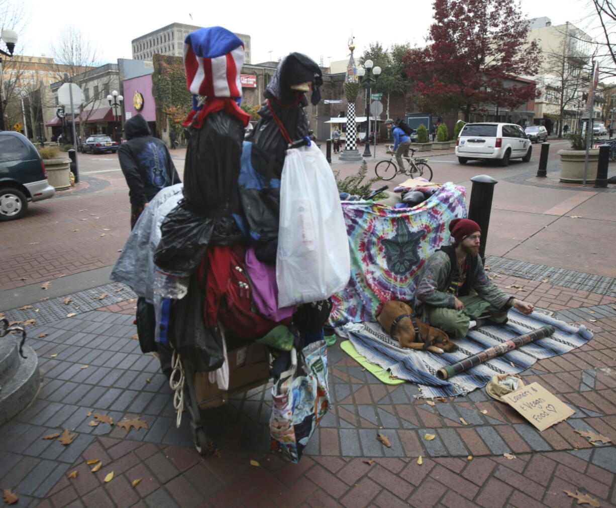 A visitor hauls a cart full of belongings through downtown Eugene, left, past another visitor asking for money at Broadway and Willamette in Eugene, Ore.  A wave of complaints about aggressive dogs in the downtown area of Oregon&#039;s third most populous city has prompted Eugene city councilors to ban dogs from the downtown area except those owned by people who live or work there.