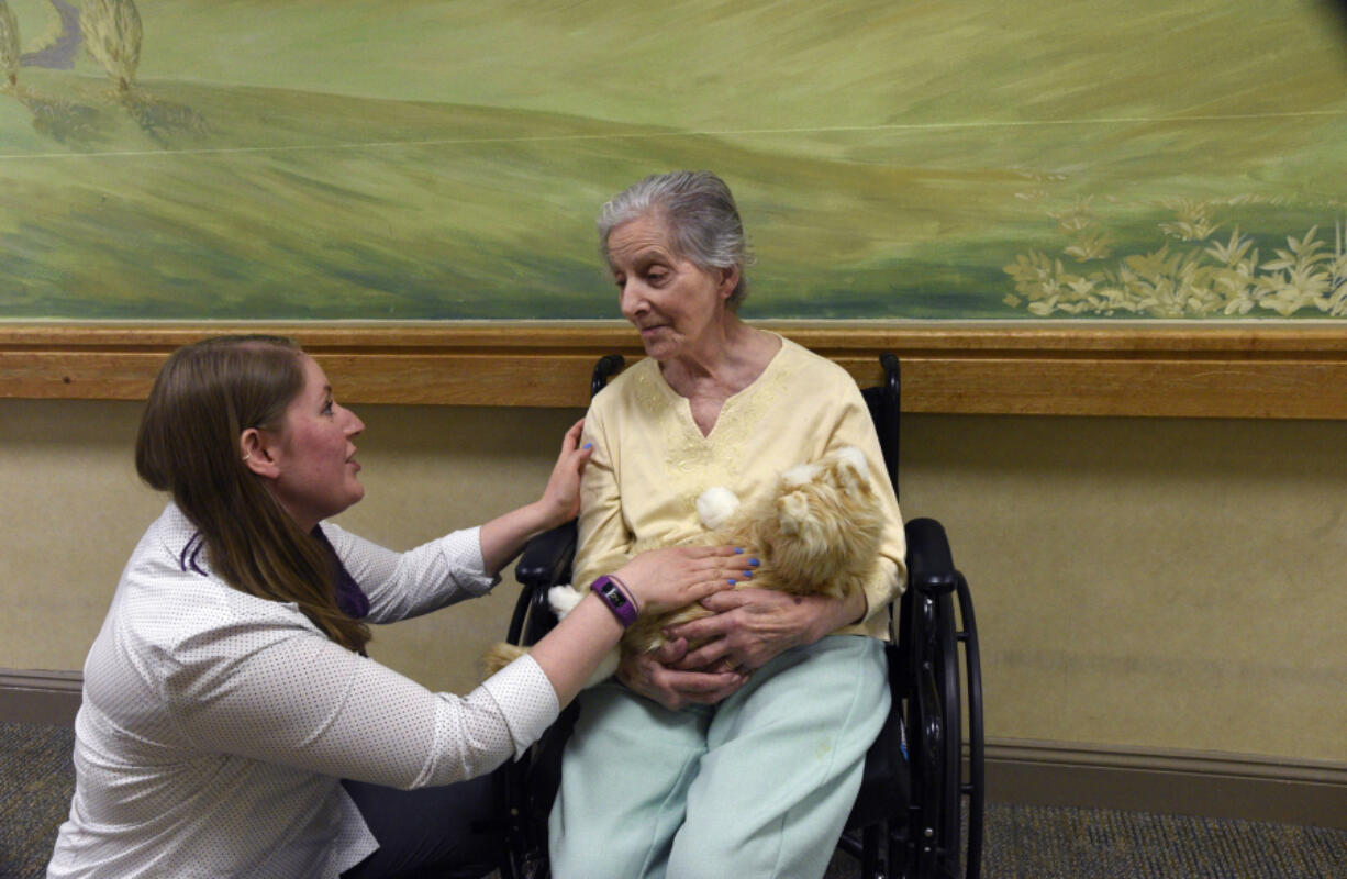 Heather Kennedy, community life director of the Glen Meadows Retirement Community, places &quot;Henry,&quot; a robotic cat, in the arms of resident Mary Thompson. The companion cat responds to petting.