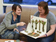 Monika Spykerman, left, looks at Jamie Morris&#039; artistic project, based on scenes and themes from the book &quot;The Interestings,&quot; by Meg Wolitzer, during book club at the Camas Public Library.