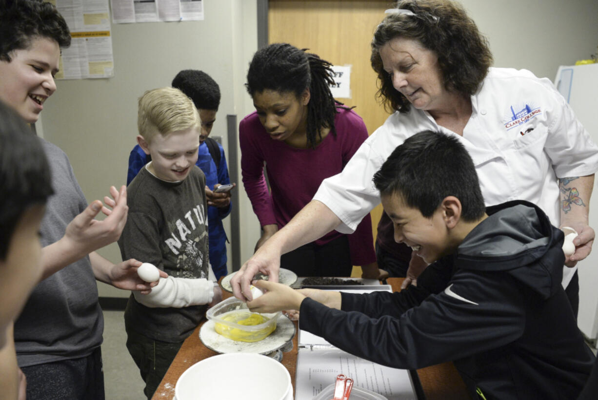 Alison Dolder, the department head for professional baking and pastry arts at Clark College, helps sixth-grader Eduardo Castellon crack an egg while Eduardo Santos, left, Jaden Cleere and Janoah Stegall watch during a baking lesson at the Boys &amp; Girls Club O.K. Clubhouse in Vancouver&#039;s Bagley Downs neighborhood.