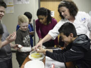 Alison Dolder, the department head for professional baking and pastry arts at Clark College, helps sixth-grader Eduardo Castellon crack an egg while Eduardo Santos, left, Jaden Cleere and Janoah Stegall watch during a baking lesson at the Boys &amp; Girls Club O.K. Clubhouse in Vancouver&#039;s Bagley Downs neighborhood.