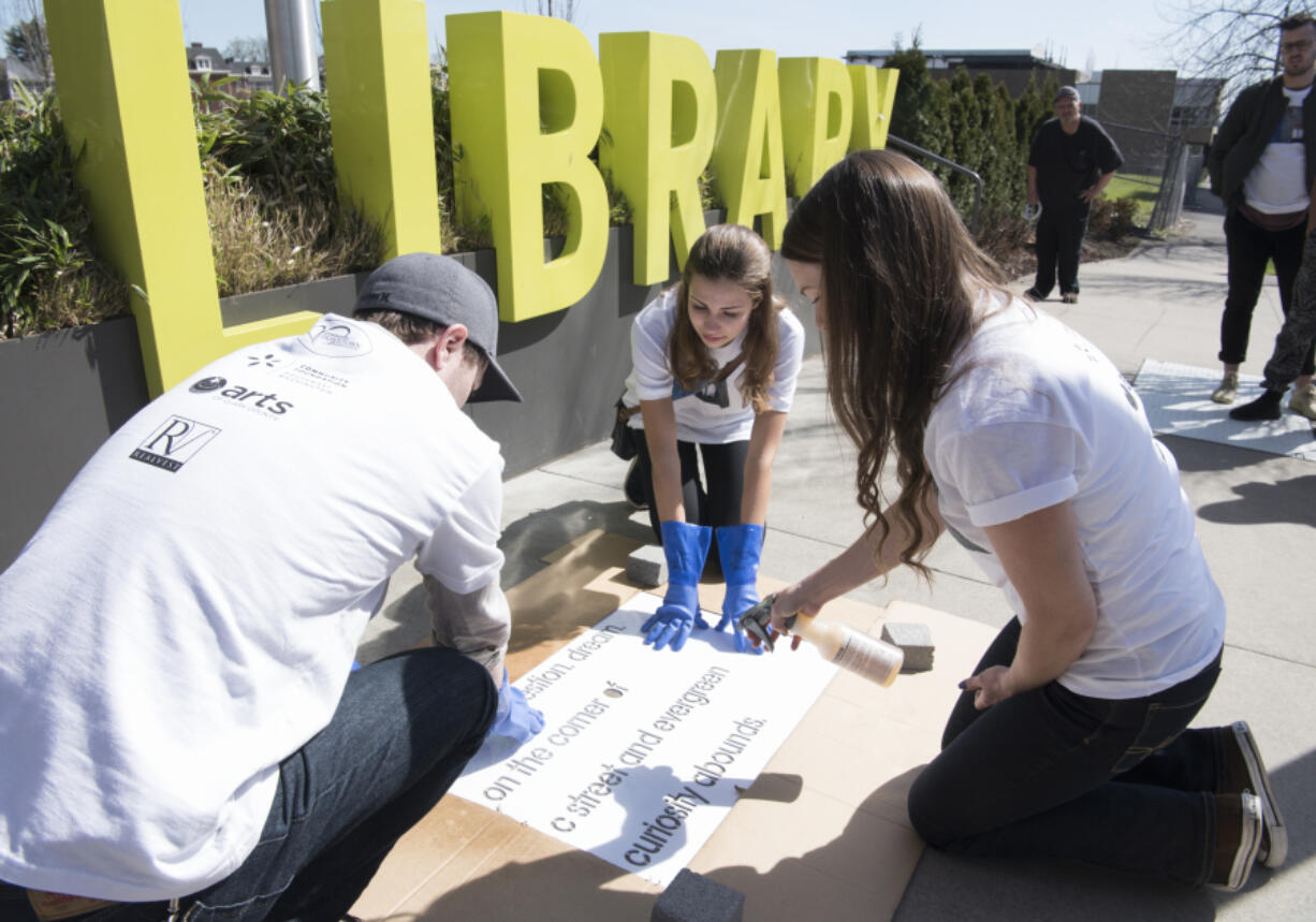 Vancouver&#039;s Downtown Association volunteers Trevor Chayce, from left, Greta DuBois and Morgan Hutchinson spray an invisible solution over a stencil of Hutchinson&#039;s library-loving poem, &quot;Gather. Question. Dream,&quot; on Friday afternoon. It&#039;s one of 24 poems that were painted on downtown sidewalks in honor of National Poetry Month.