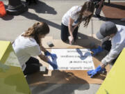 Volunteers for Vancouver&#039;s Downtown Association  Greta DuBois, left, Morgan Hutchinson and Trevor Chayce spray an invisible solution over a stencil of Hutchinson&#039;s library-loving poem, &quot;Gather. Question. Dream,&quot; last Friday afternoon. It&#039;s one of 24 poems that were painted on downtown sidewalks in honor of National Poetry Month. The trick is, you can only see the poems when the weather is wet - but in this part of the world, that shouldn&#039;t be a problem.