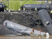 FILE - In this May 1, 2014, file photo survey crews in boats look over tanker cars as workers remove damaged tanker cars along the tracks where several CSX tanker cars carrying crude oil derailed and caught fire along the James River near downtown Lynchburg, Va. Inspectors have found almost 24,000 safety defects over a two-year period along United States railroad routes used to ship volatile crude oil. Data obtained by The Associated Press shows many of the defects were similar to problems blamed in past derailments that caused massive fires or oil spills in Oregon, Virginia and Montana.