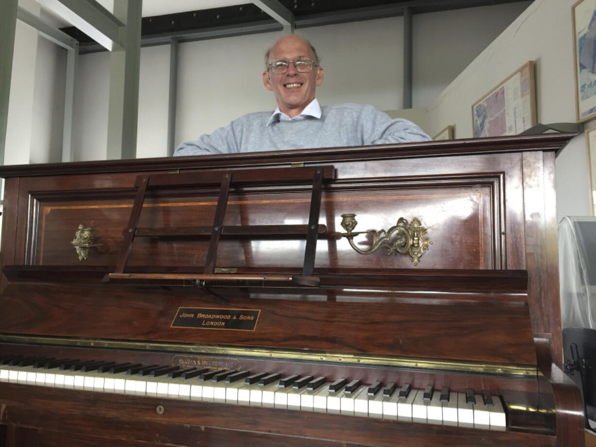 Piano tuner Martin Backhouse with the piano where he found a stash of gold, smiles in Ludlow Museum in Ludlow, England, on Thursday.