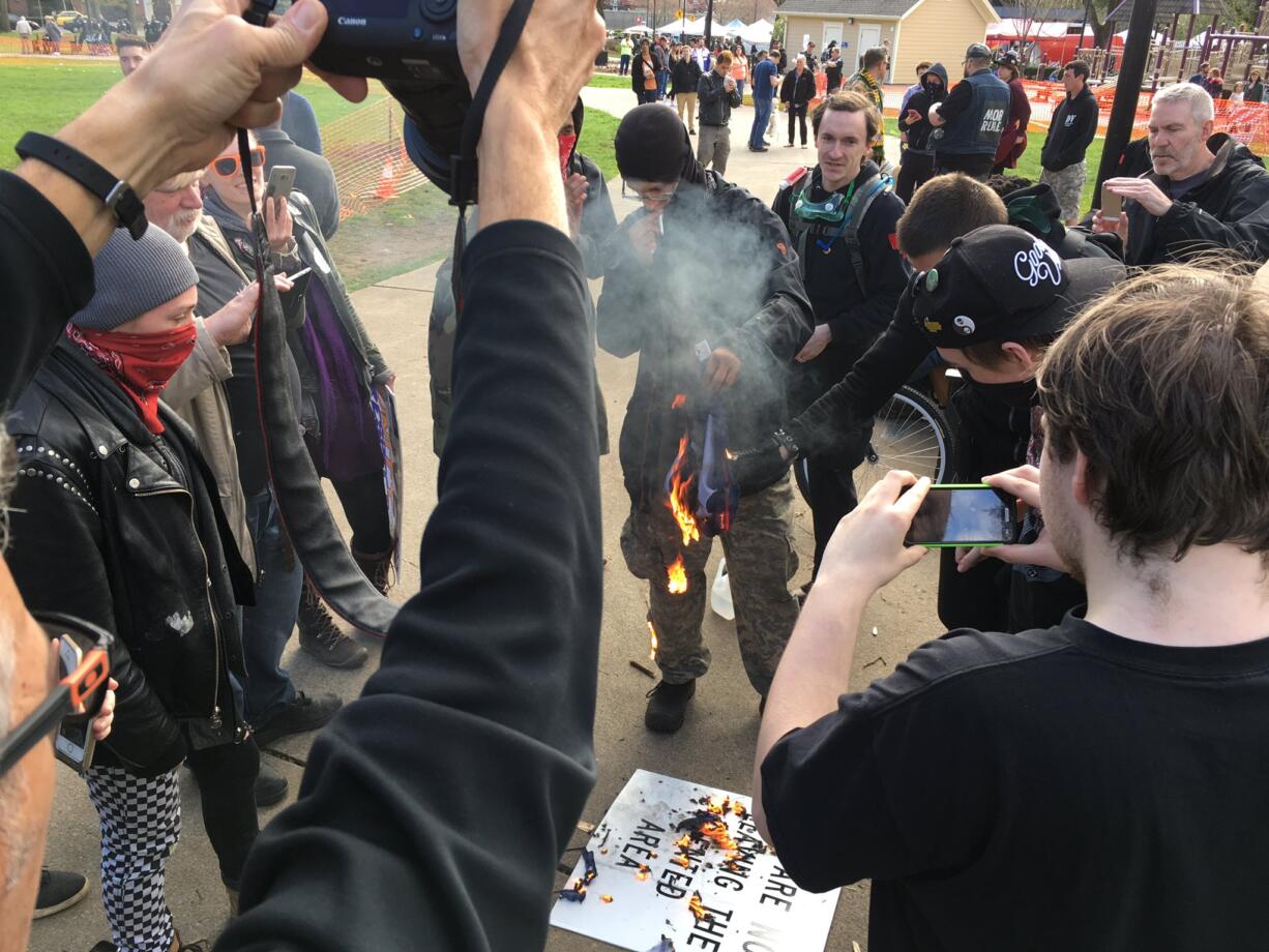 Trump opponents, dressed in black, set fire to a Trump/Pence campaign flag and a sign.