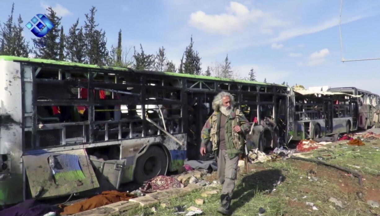 This frame grab from video provided by the Thiqa News Agency, shows a gunman passes by the buses that were damaged in a blast at the Rashideen area, a rebel-controlled district outside Aleppo city, Syria, Saturday, April. 15, 2017. Syrian TV said at least 39 people were killed Saturday in an explosion that hit near buses carrying evacuees from two towns besieged by rebels nearby.