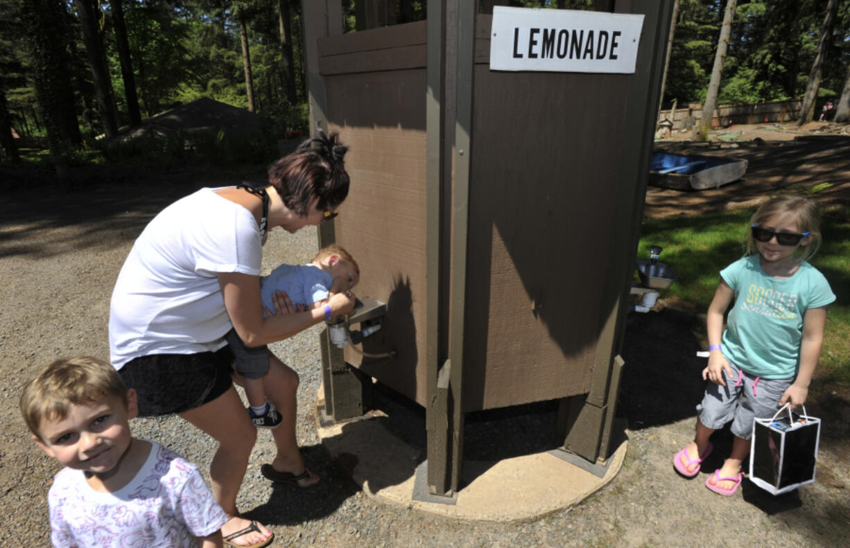 Kolton Groth, left, stands nearby as his brother Cooper, held by Tanya Groth, enjoys some pink lemonade at the fountain at Alderbrook Park in Brush Prairie. The private park, which first opened for events in the 1960s, has been known locally for the lemonade fountains.