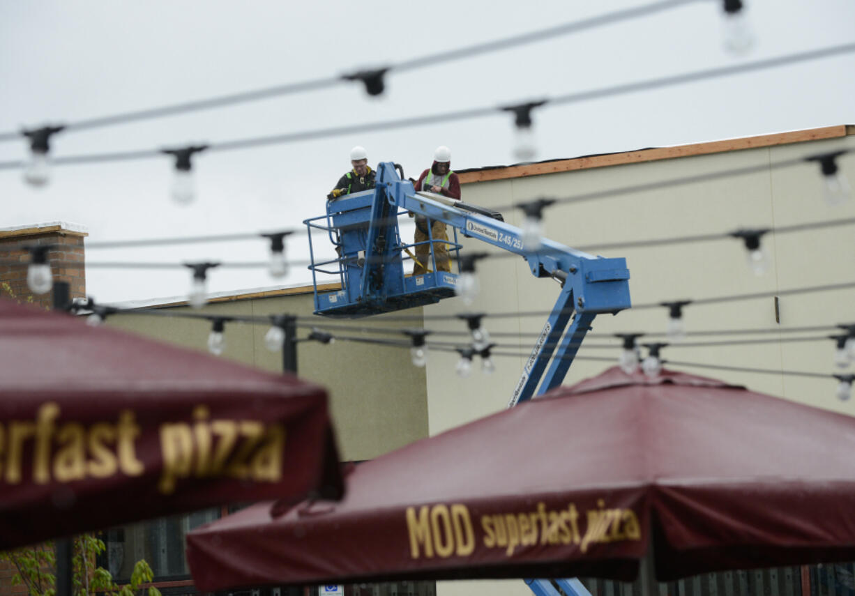 A construction crew at Hazel Dell Marketplace is seen through string lights at Mod Pizza. A mix of tenants, including retail, food and even healthcare, has helped grow the shopping center, according to developers.