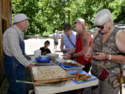 Kurt Friedmann, left, offers his fry bread to visitors as the Cedar Creek Grist Mill, built in 1876, opens its season Saturday northeast of Woodland.