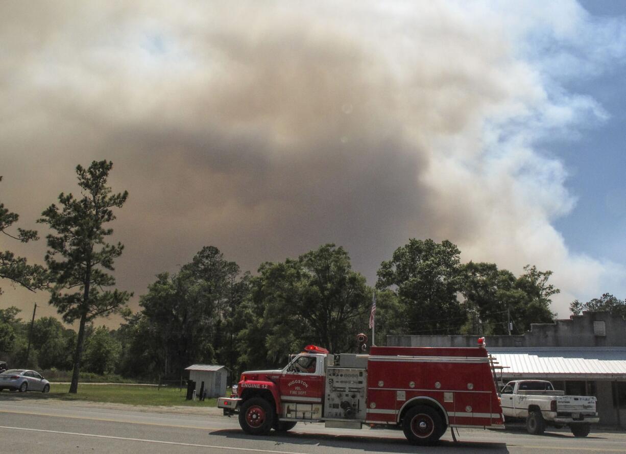 A fire truck passes as a plume of smoke rising from a wildfire burning, Monday, May 8, 2017, just outside the town of St. George, Ga. Officials placed the town under a mandatory evacuation after winds pushed the fire out of the neighboring Okefenokee National Wildlife Refuge, where a lightning strike started the blaze a month earlier.