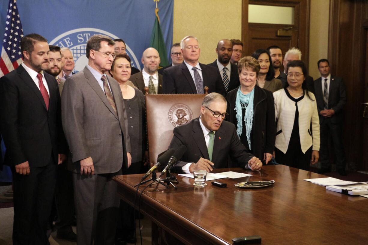 Gov. Jay Inslee, seated, prepares to sign a bill that seeks to bring Washington state into compliance with the federal REAL ID Act, on Tuesday, May 16, 2017, in Olympia, Wash. The federal law requires state driver's licenses and ID cards to have security enhancements and be issued to people who can prove they are legally in the United States.