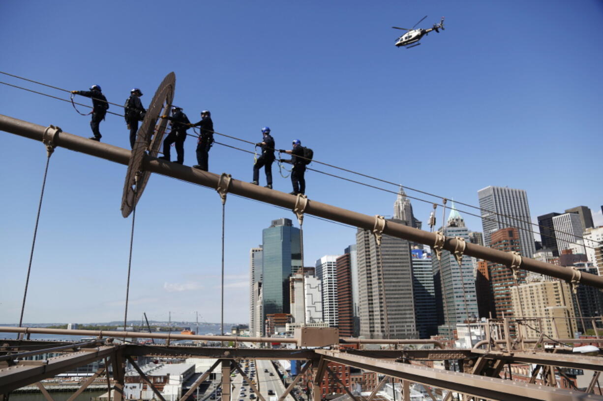 A NYPD helicopter flies overhead as New York City police officers, including members of the Emergency Services Unit, walk up a cable to the top of the Brooklyn Bridge in New York. The 400-team unit,  an elite group of officers trained to handle the city???s most dangerous rescues, trains for months not only on technical rescue techniques, but also on how to talk to people to get them down safely.