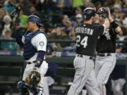 Chicago White Sox's Matt Davidson (24) is greeted by Todd Frazier, right, as Seattle Mariners catcher Carlos Ruiz, left, looks on after Frazier scored on a home run hit by Davidson in the seventh inning of a baseball game, Saturday, May 20, 2017, in Seattle. (AP Photo/Ted S.