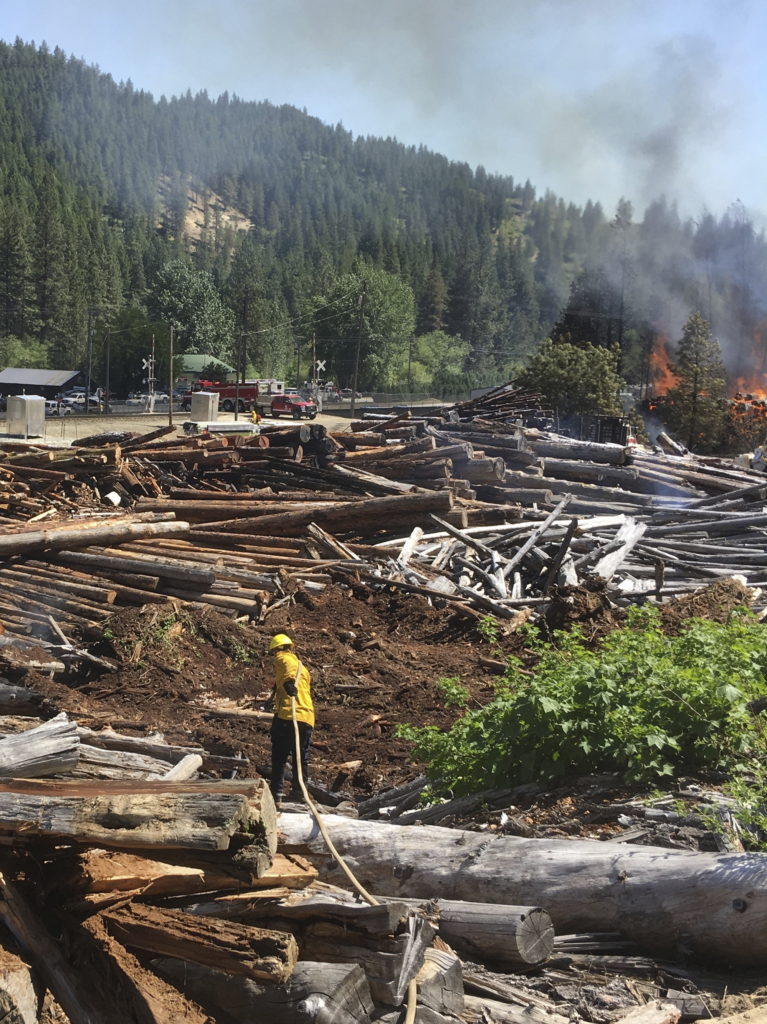 In this May 23, 2017 photo provided by Chelan County Fire District 3, a firefighter works as a portion of a pile of logs burns near Leavenworth, Wash. The wildfire that started at an old log-storage site has prompted evacuation orders for homes and cabins at a popular Washington state hiking and skiing destination, officials said Wednesday.