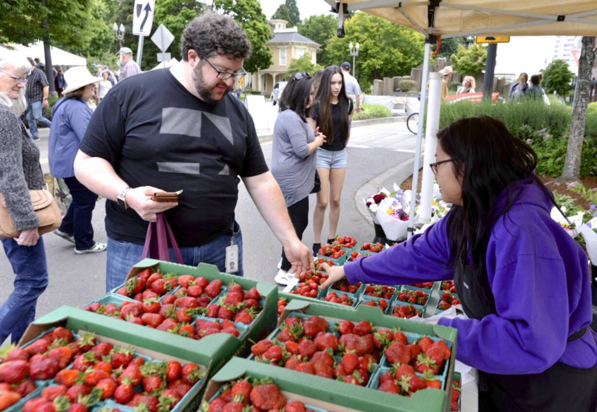 Greg Landweber, left, buys strawberries from Mai Yang at the farmers market in Vancouver Sunday. Lingering cold weather and rainfall into spring meant a later crop for many regional strawberry growers.