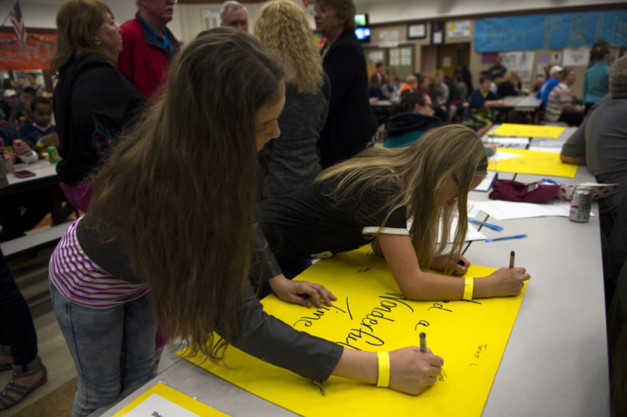 Jemtegaard Middle School sixth-graders Sophia Young, left, and Lily Barrett, sign their names on commemoration posters during the school district’s One Last Time celebration to say goodbye to the school building, which opened in 1981 and will be demolished this summer.