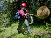 Larch Corrections Center inmate Eric Rodriguez unfurls a rolled hose during a training exercise for the prison’s wildland firefighting program. Larch has an inmate work crew that fights fires and works on land management projects around the region.