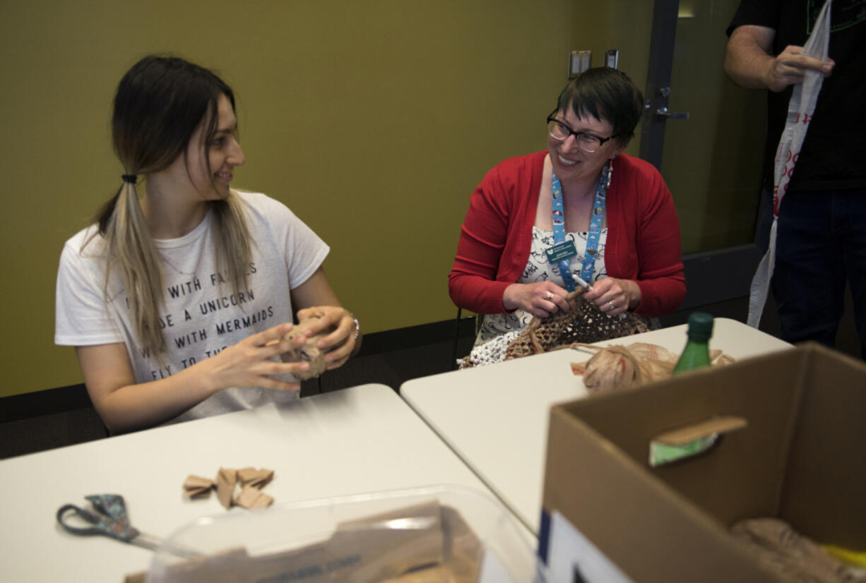 Volunteer Deanna Harper, left, creates plastic yarn balls, or plarns, and chats with librarian Jamie Bair, who crochets a plastic sleeping mat Tuesday evening at the downtown Vancouver Community Library. Kicking off the summer’s Make a Better World series, this event helped prepare the plastic yarn balls that will be crocheted into sleeping mats for homeless people.