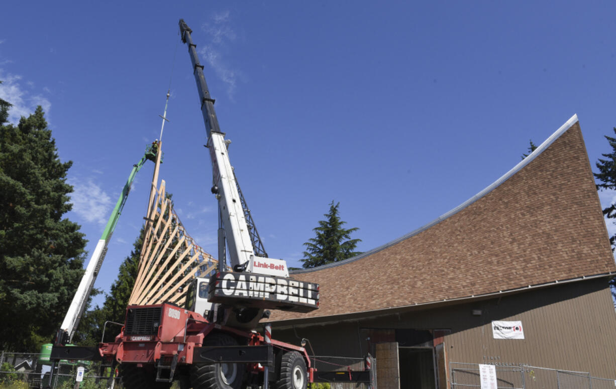 A crane holds a cross over the roof of First Congregational United Church of Christ in Hazel Dell while workers in a construction basket secure it into place.