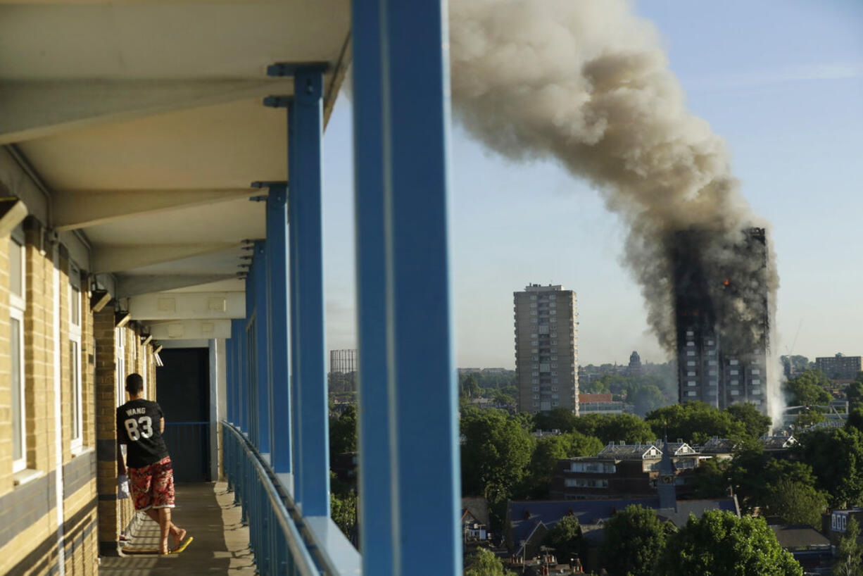 A resident in a nearby building watches smoke rise from a building on fire in London, Wednesday, June 14, 2017. A massive fire raced through the 27-story high-rise apartment building in west London early Wednesday, sending at least 30 people to hospitals, emergency officials said.