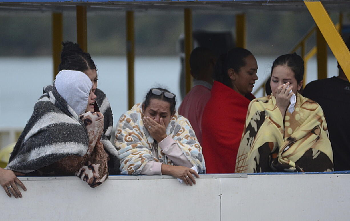 People who survived a sunken ferry, cry as they wait for more information about their missing friends and relatives, at a reservoir in Guatape, Colombia, on Sunday. Nine people were dead and 28 missing after a tourist ferry packed with around 170 passengers for the holiday weekend capsized Sunday on a reservoir near the Colombian city of Medellin, officials said.